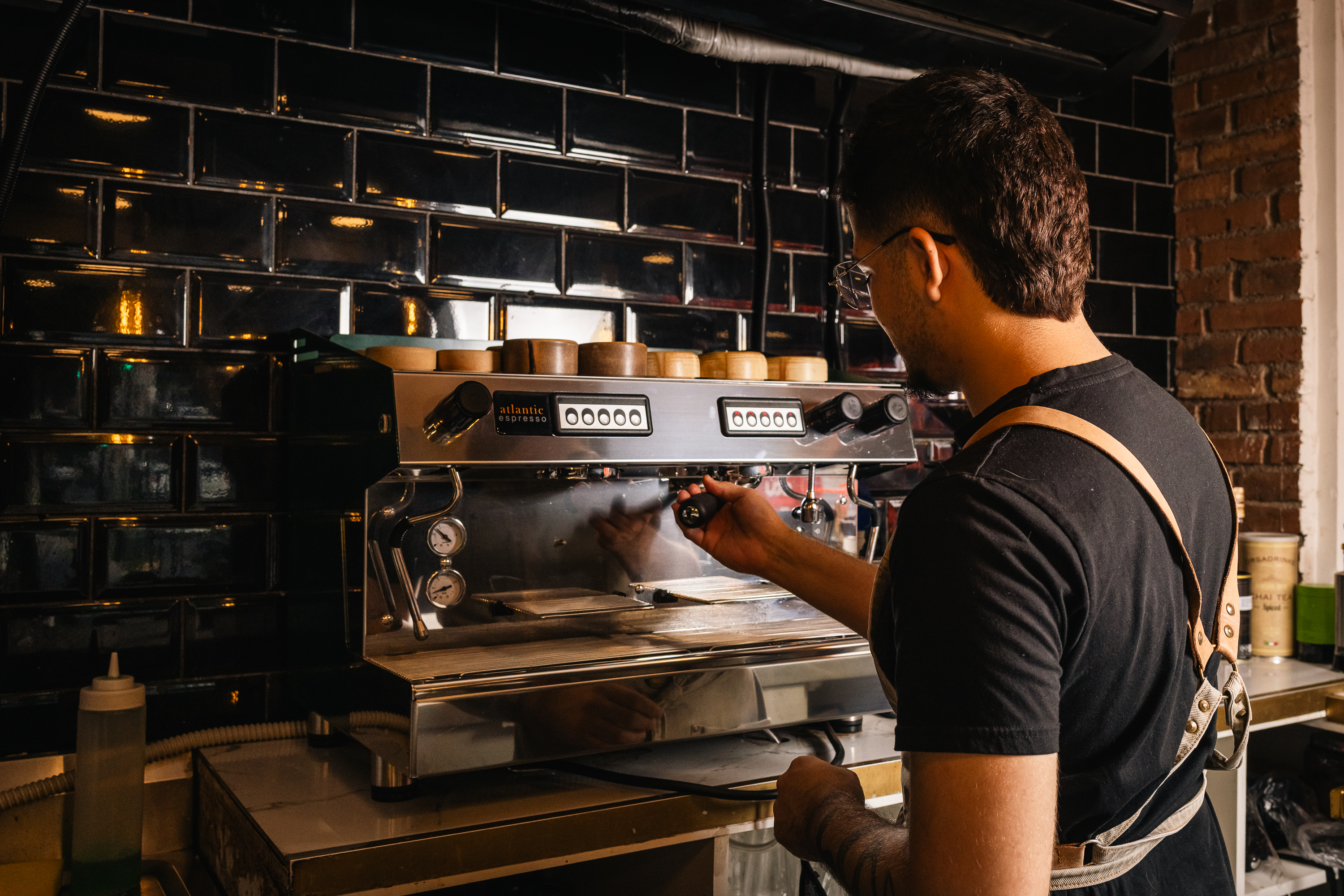 Barista preparando café en la máquina, frente al muro de ladrillo